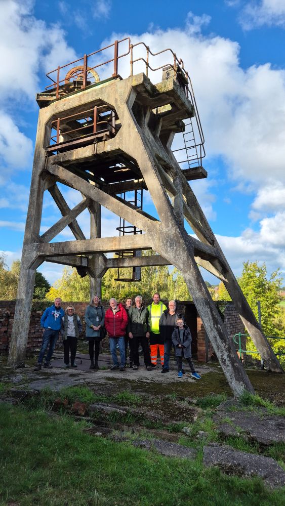 Group of nine people standing under the remaining pithead gear (part of the winding mechanism for the mineshaft lifts) at Hemingfield Colliery.
