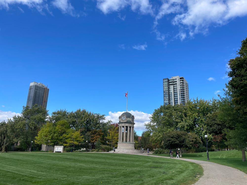 Victoria Park Kitchener - clock tower and pathway under blue skies with some clouds. Taken Oct 8, 2025 so some of the leaves are changing colour 