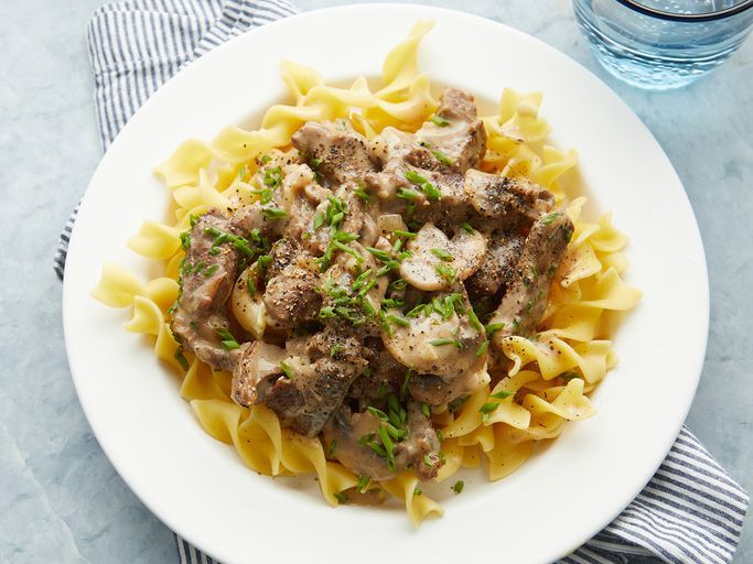 close up on a bowl of classic beef stroganoff over pasta, garnished with fresh herbs 