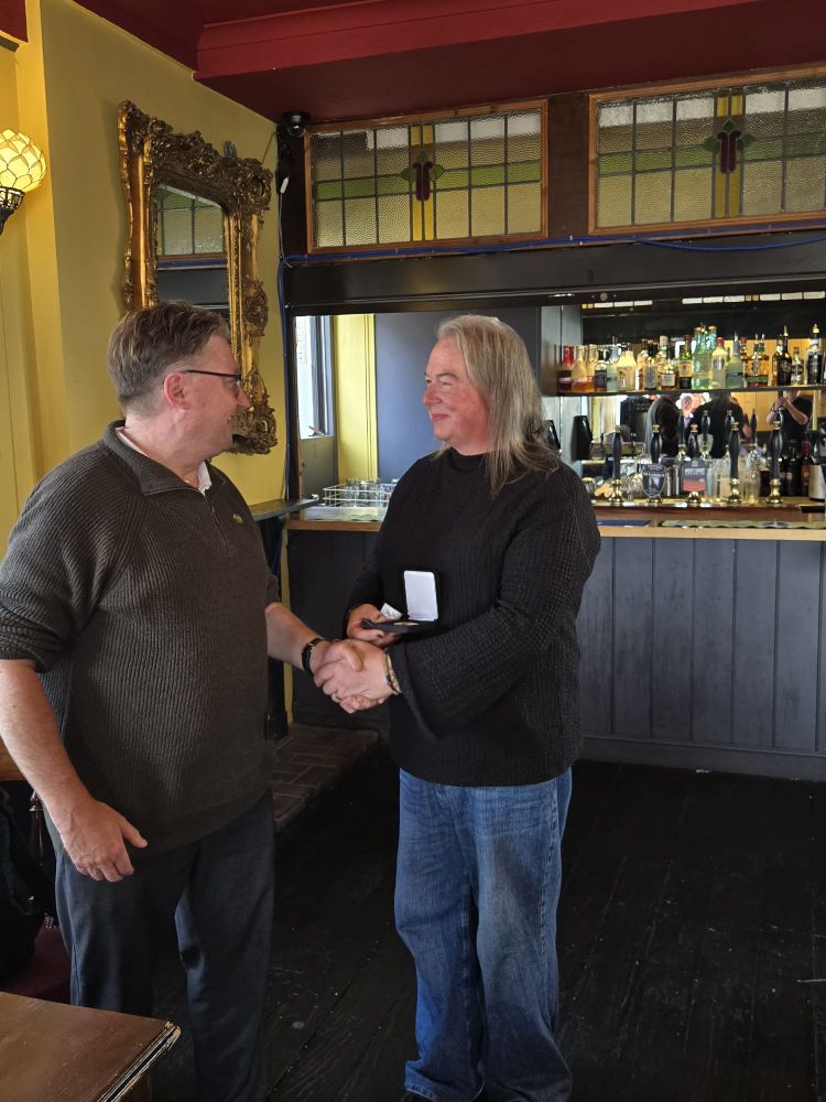 Two people shaking hands inside a cozy pub with a bar stocked with bottles and taps in the background.