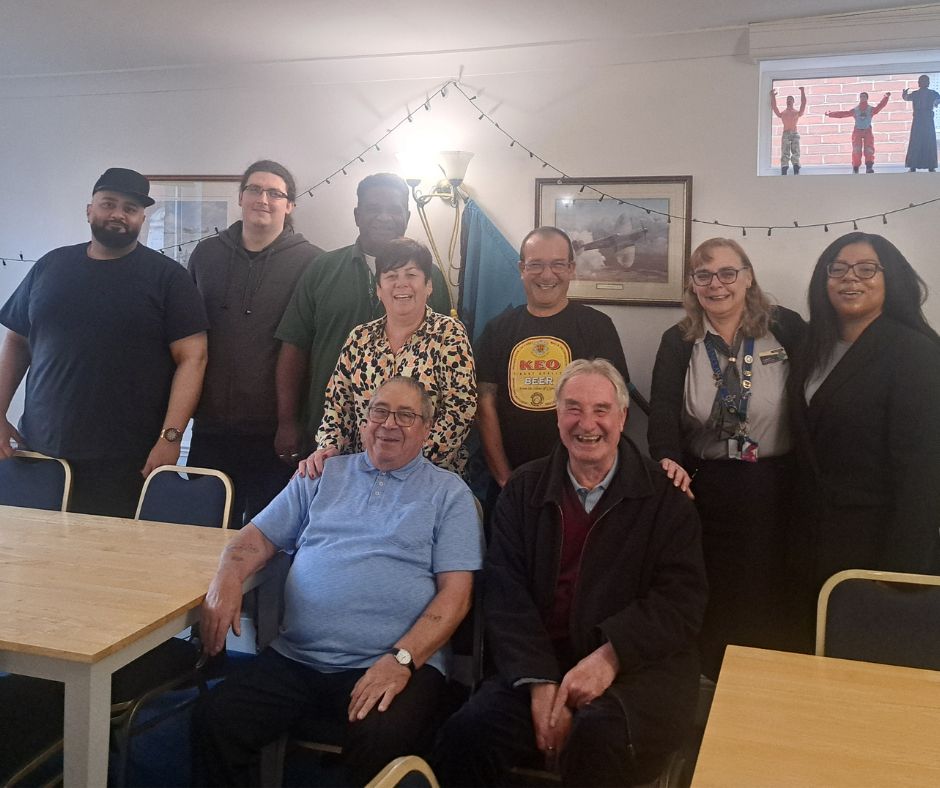 Group of nine RMT members posing indoors around tables with framed pictures and string lights on the wall behind them.