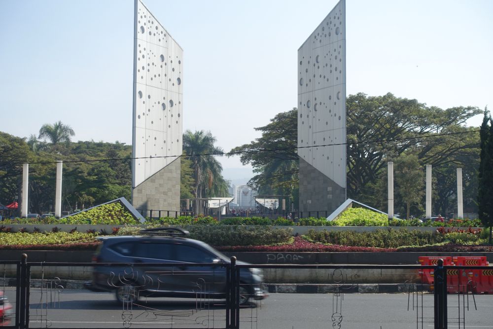 2 witte 15 meter hoge monumentale stenen op een plein met een autoweg er om heen.  In de stenen zitten ronde gaten van verschillende grote. 