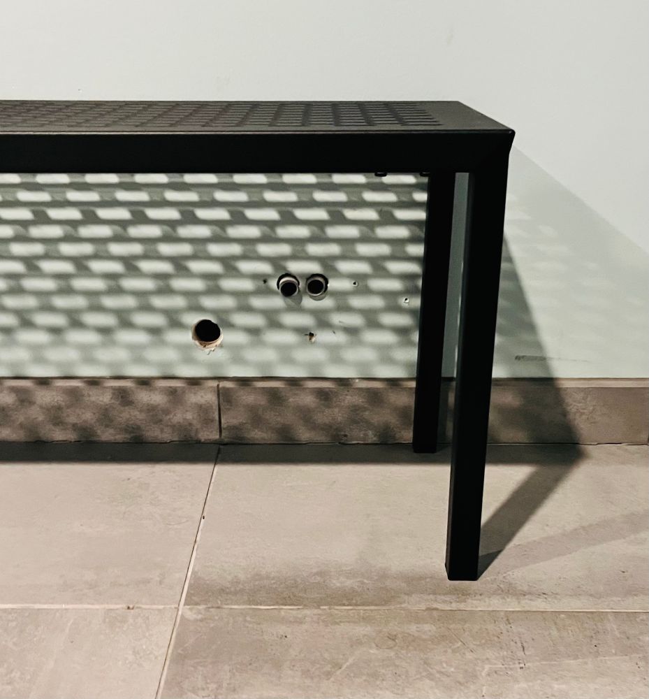 A wall with holes under a bench, resembling a face with wide eyes and an O:shaped mouth.