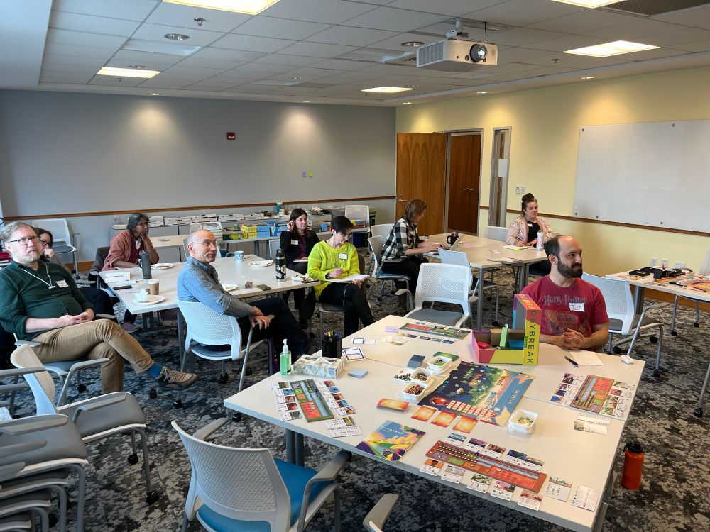 Conference room with Daybreak (board game) set up in front and audience listening to Matt Leacock talk to us!