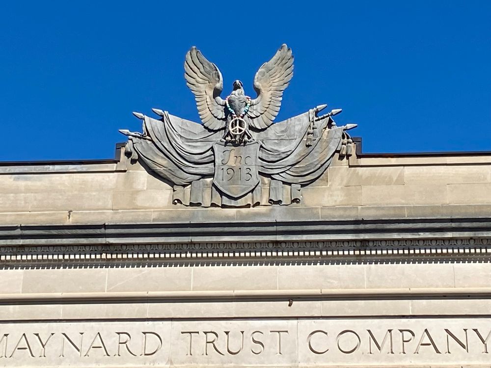 A classical stone eagle on top of the Maynard Trust Company. He’s wearing a little peace sign around his neck