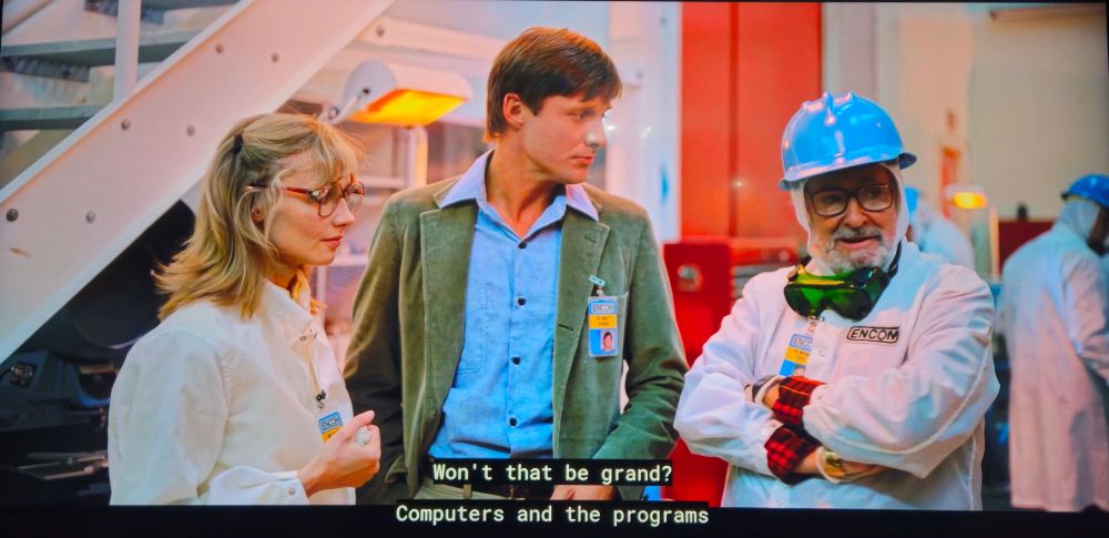 Image of three people talking in the 1982 film Tron, with on saying "won't that be grand.  Computers and the programs"