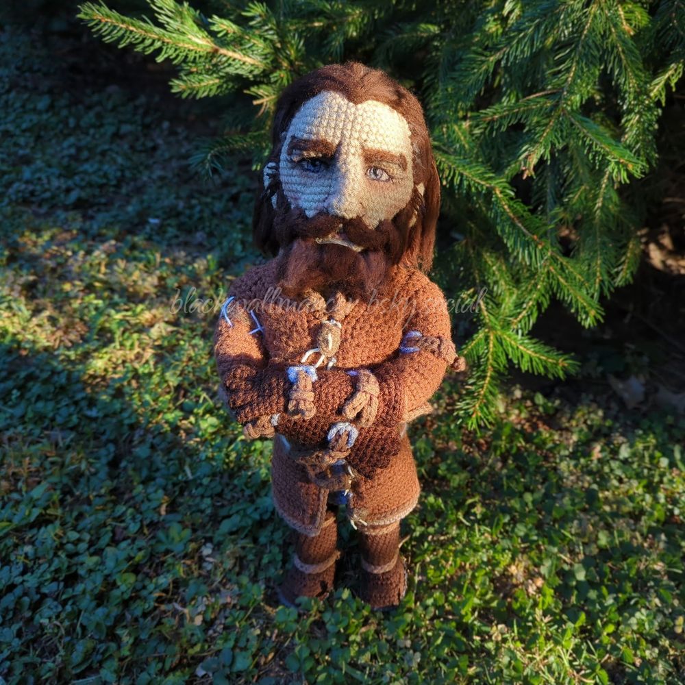 A highly detailed Blackwall (Dragon Age Inquisition) amigurumi, standing outside in the morning light. Behind him are the branches of a pine tree. His arms are folded across his chest, and his needle felted eyes are looking up and into the camera. No pattern—freehanded. More pics and info about how I made him here (see alt text): https://bsky.app/profile/blackwallmancer.bsky.social/post/3lz6zem7bik2w