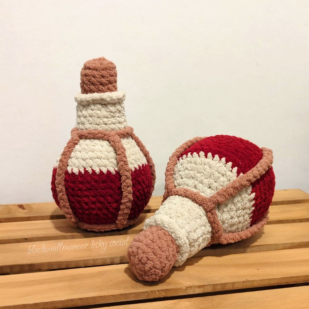 Two plushies made to look like potion bottles half filled with red fluid. In this photo, one bottle is standing up, while the other is lying on its side. The bottles are crocheted with blanket yarn in red, off-white, and brown. Both bottles have a cork sewn into the neck.

Pattern modified from ThePointedHat.