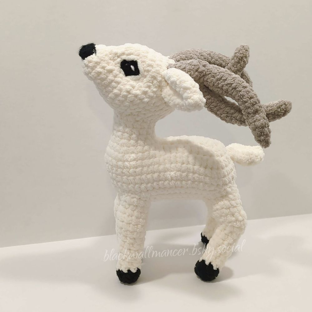 A crocheted Halla—a white fantasy deer with black hooves, eyes, and nose and intertwining grey antlers—posed on a white backdrop and facing to the left.

modified from the pattern "Darcy Deer" by Valerie Church.