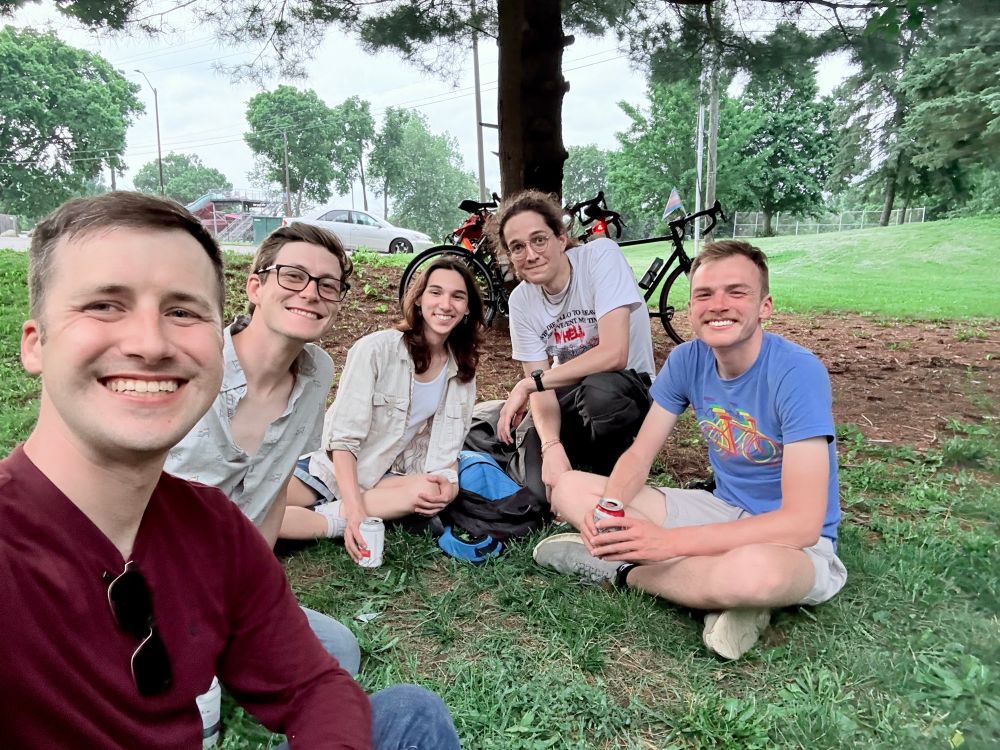 A photo of 5 people sitting on the grass in front of a tree with bikes leaning against the tree. From left to right are Brandon, Matt Weiss, Riley Choe, @rustbeltenjoyer and Will Hazen