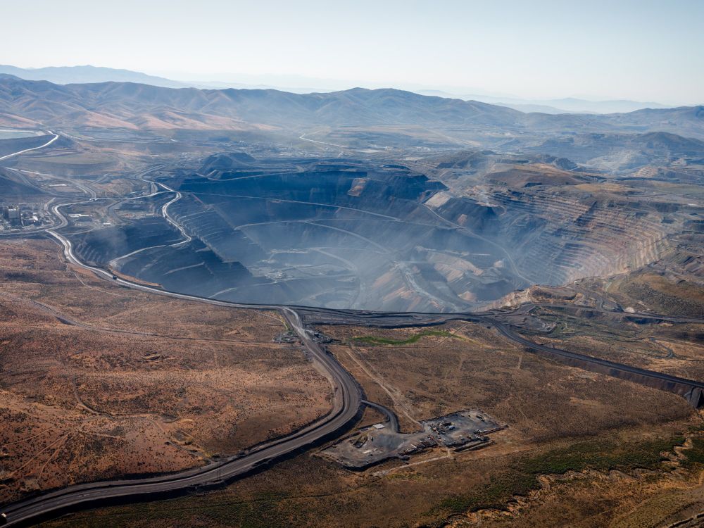 An aerial photo shows a massive open pit mine with haze rising from the center.

