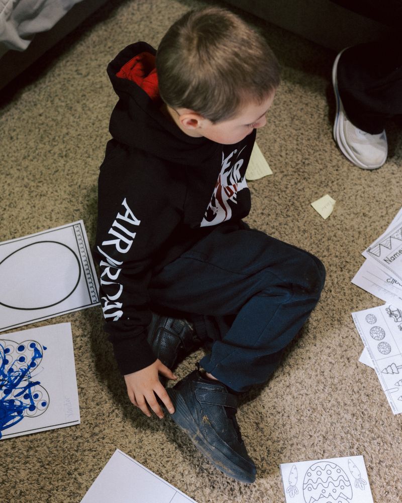 A photo of a boy seated on a carpet surrounded by paper craft pages.