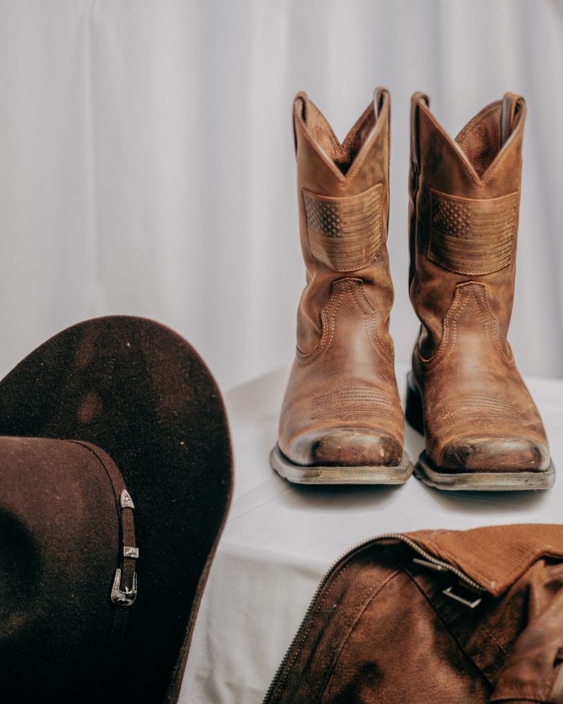 A pair of cowboy boots, a cowboy hat, and a piece of leather clothing.