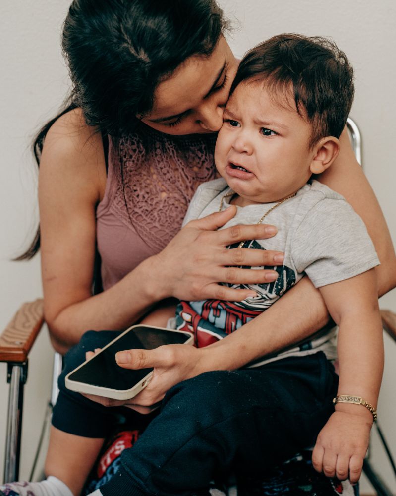 A woman holding a crying child on her lap while seated in a chair. 
