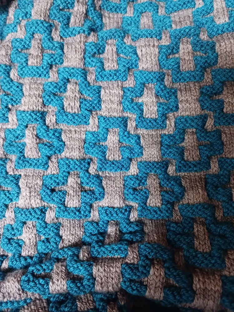 Blue raised garter stitch crosses on a gray stockinette stitch background 