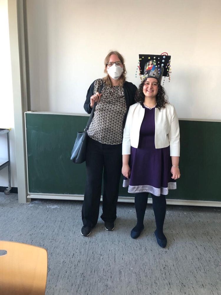Me (a dark-blond tall woman) and Eshita (black-haired woman) in front of a black board at the university, happy after her successful defense. She is wearing her PhD hat with pictures, particle string made of wooden pearls and pipe-cleaner vortices to represent turbulence.