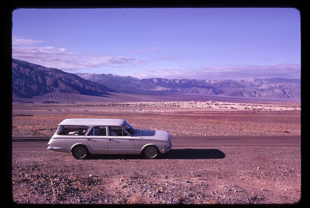 Far flat plain of dusky browns with white 60s station wagon in the foreground. 