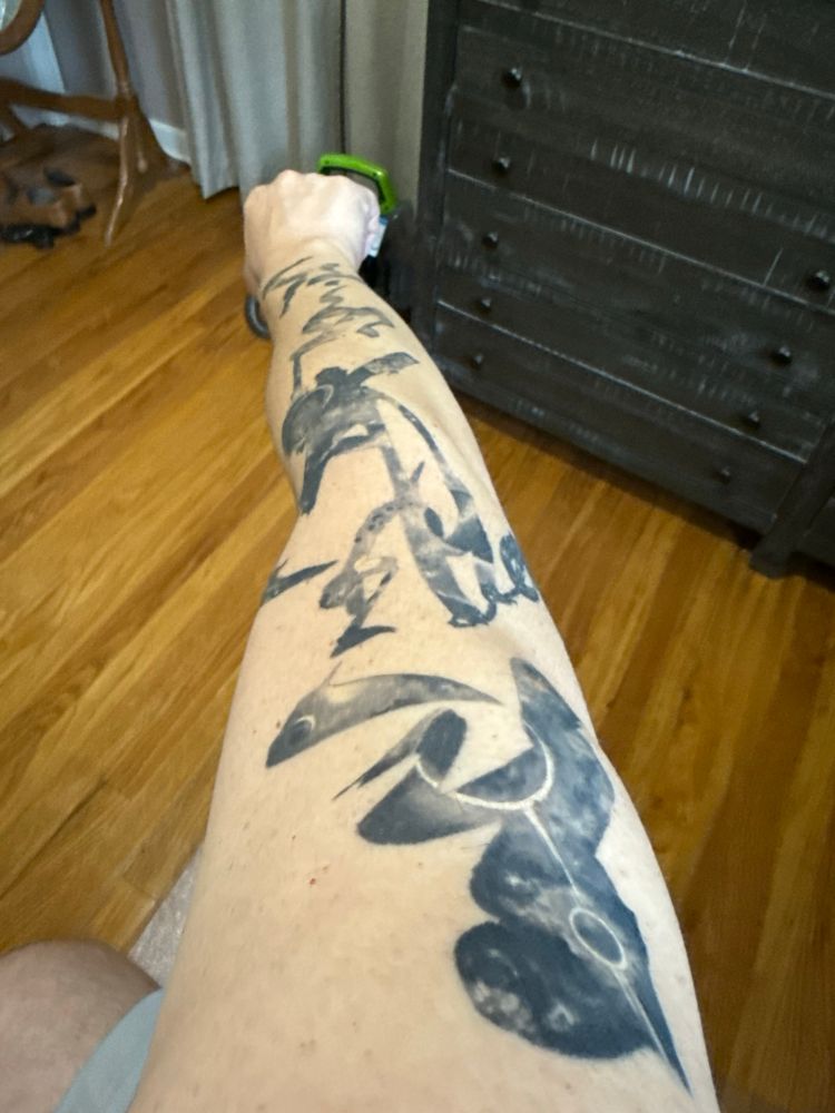 A dumbass’s right arm extended showing an extensive tattoo in brush-work outlining the galaxy. 