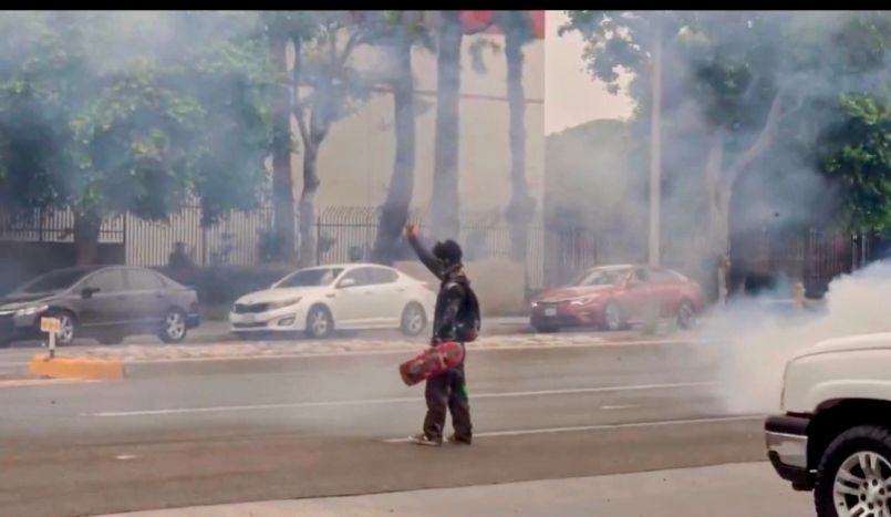 Still frame of skater dude flipping off ICE admits flash bangs smoke surrounding him. 