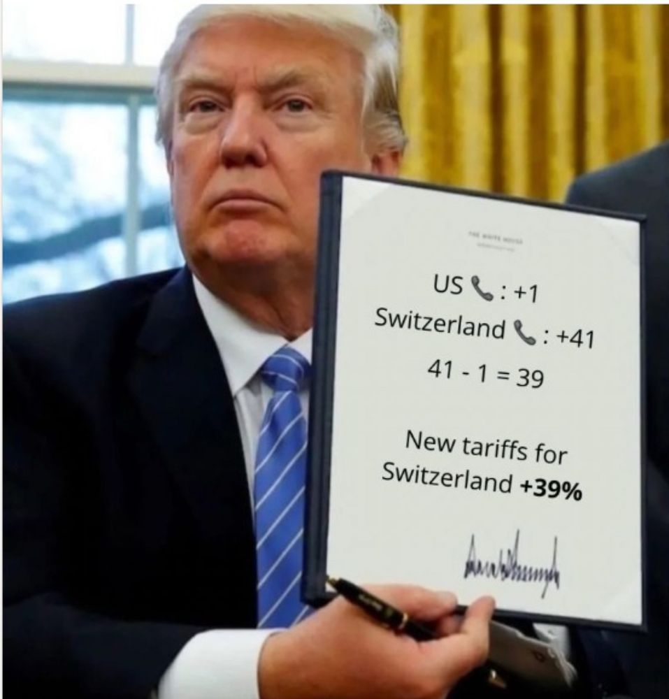 Taco hält eine seiner Ankündigungen in der rechten Hand mit dem Text:

US 📞 : +1
Switzerland 📞: +41
41 - 1 = 39
New tariffs for Switzerland +39%

