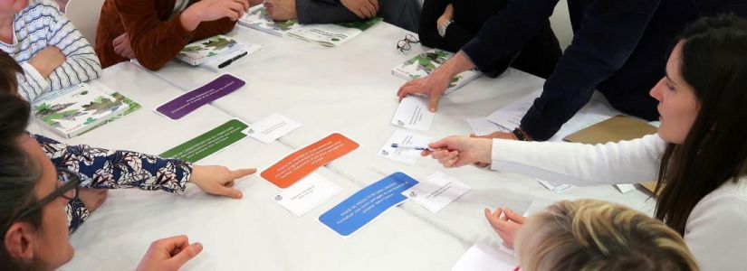 Autour d'une table où se trouve des textes imprimés sur des étiquettes, un groupe semble discuter en pointant des étiquettes différentes