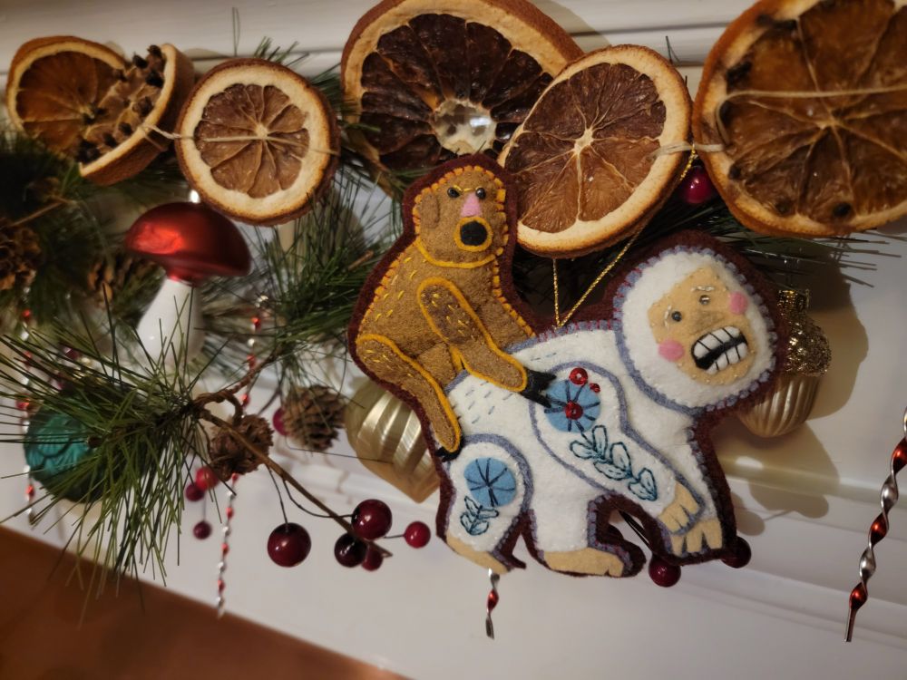 A closeup of the garland on my mantle. The focal point is a handmade felt ornament of the "Season's Greason's" meme, which is of a monkey-like creature attacking a yeti-like creature.