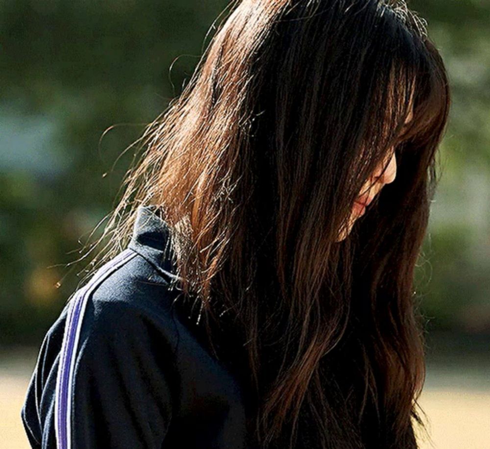 a woman with long dark hair is wearing a black jacket with blue stripes on the side