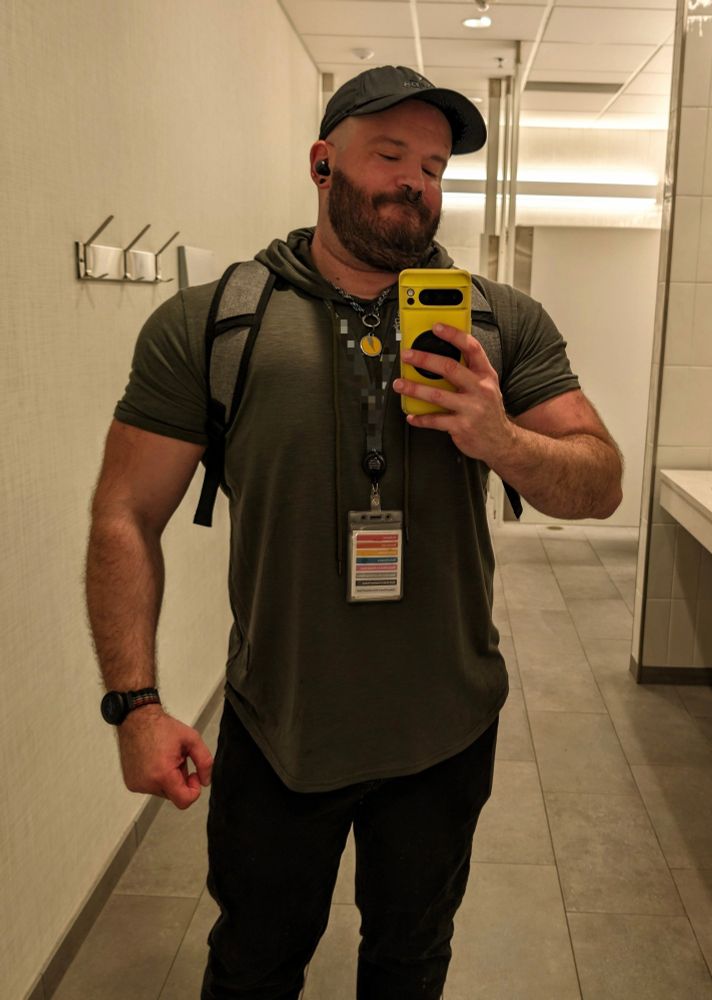 Front-facing shot of a guy in a forest green short-sleeve hoodie, black jeans, and a black ball cap.