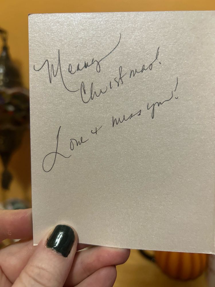 A  hand holds up a Christmas card with a handwritten message inside saying merry Christmas love and miss you