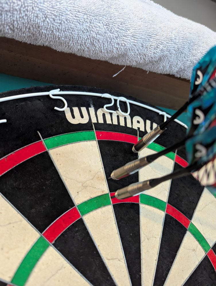 Blue-finned silvery darts are imbedded in a dartboard. Two are in the 20, one is in the treble 20