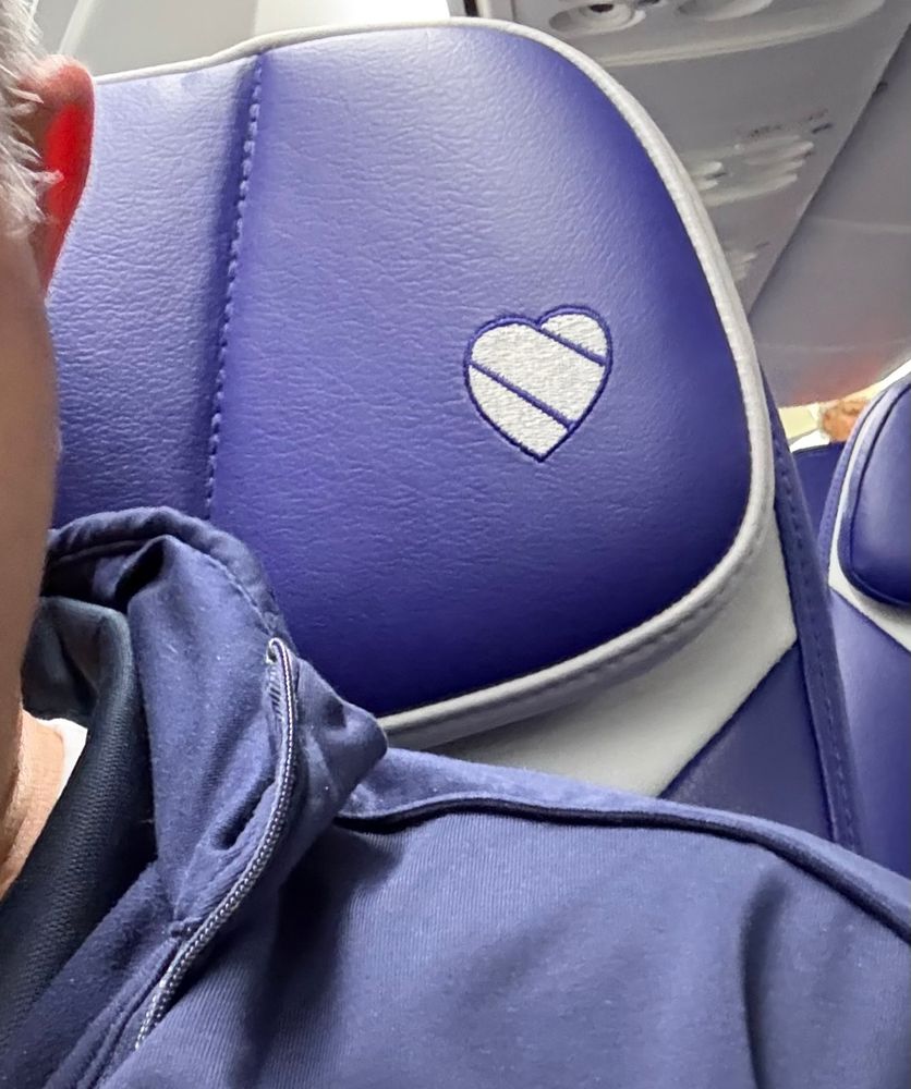 Close-up of a person’s shoulder while sitting in a Southwest Airlines seat. The purple and white headrest features the airline's embroidered heart logo