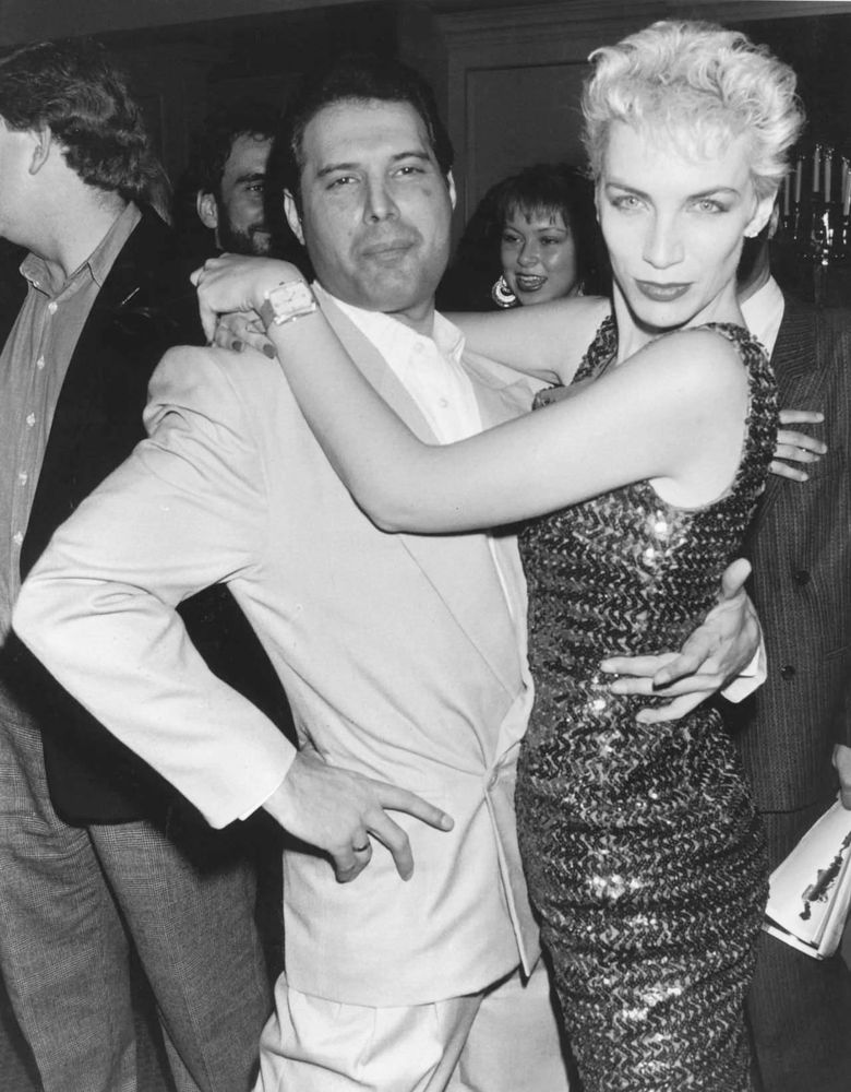 Een zwartwit foto van Freddie Mercury en Annie Lennox in omhelzing, Annie Lennox heeft een glitterjurk aan, en Mercury een lichtgekleurd pak. Het is een feest en ze kijken in de camera.