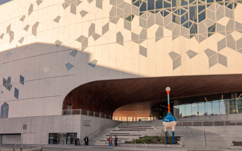a big wall of the calgary central library with a long stairway and archway and all of it cast in warm light and shadow.