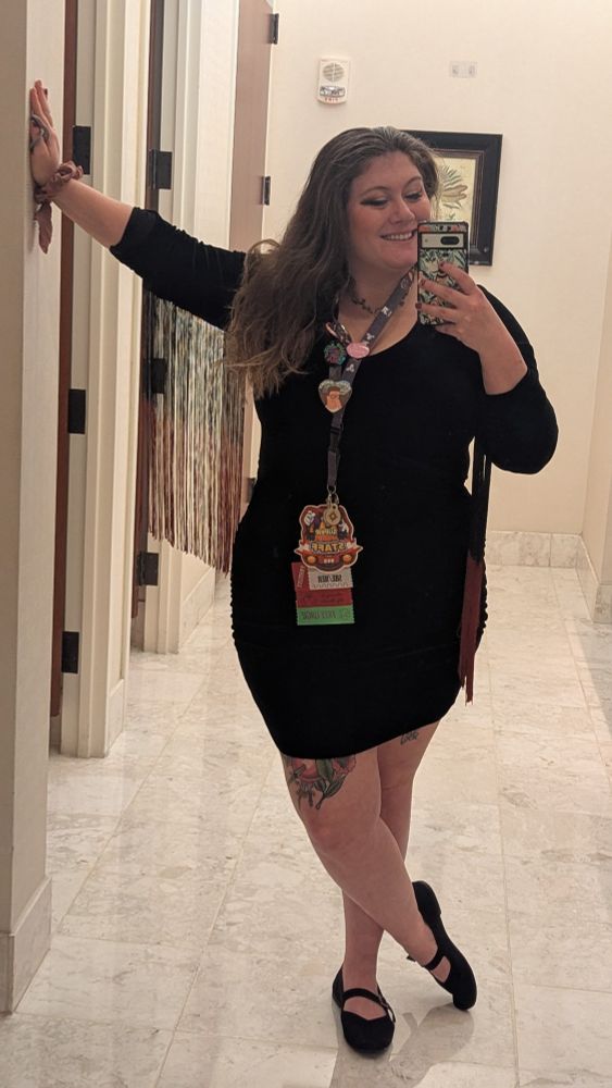 amber stands in the bathroom wearing her black Persephone dress, smiling at the camera