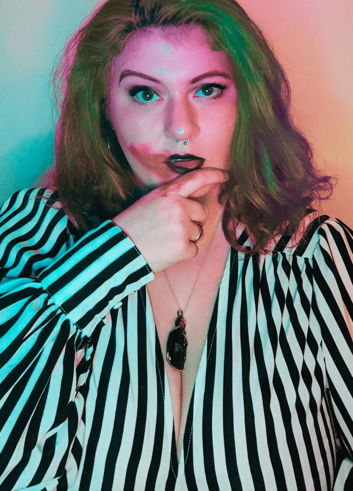 A picture of Amber from an old Vampire: the Masquerade stream. She wears a striped black and white blouse, a black pendant necklace, and is wiping (simulated) blood from her mouth.