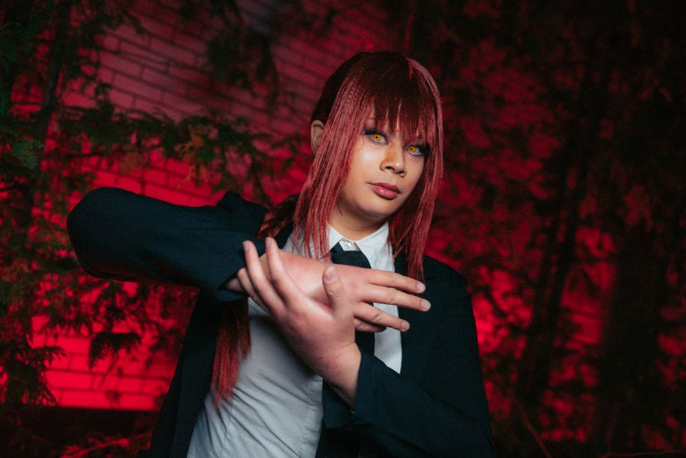 Yuuko cosplaying as Makima from Chainsaw Man, doing hand signs in front of a red illuminated wall.