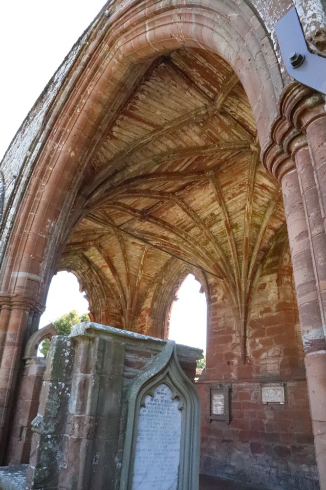 Blick durch ein altes Portal in den Innenraum einer gotischen Kirche. Die Fenster sind rausgebrochen, die Gewölbedecke aber unverputzt erhalten, kein Dachgestühl. 