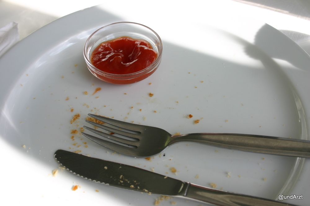 Ein leergegessener Teller mit Messer und Gabel und einem Glasschälchen mit einem Rest einer roten Substanz.