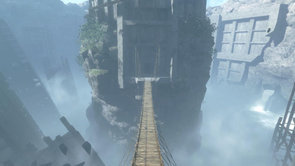 "Screenshot from NieR Replicant ver.1.22474487139.... A long, narrow suspension bridge extends towards a massive, crumbling stone structure in a misty canyon."

