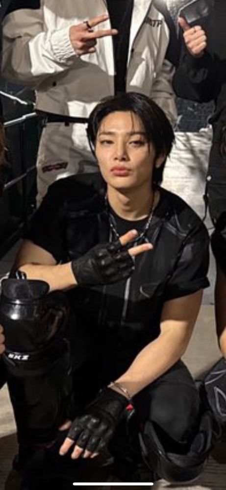 crop from stray kids group photo focused on jeongin. he is crouching doing a backwards peace sign and doing "blue steel"