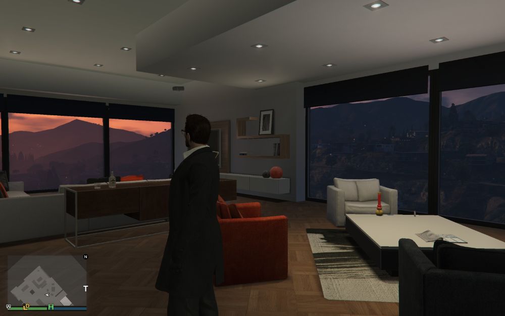 a screenshot from grand theft auto online of a guy standing in a high rise apartment with a sunset outside against the hills