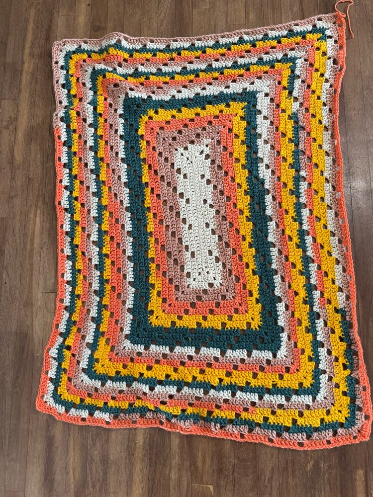 Lap blanket crocheted in white, tan,orange, green and yellow.  Spiraling gaps form a decorative pattern.