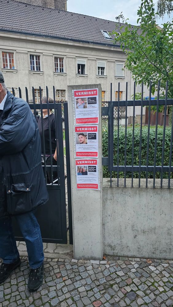 An einer Mauer hängen drei Plakate mit der Aufschrift VERMISST! und Foto und Beschreibung der Vermissten.