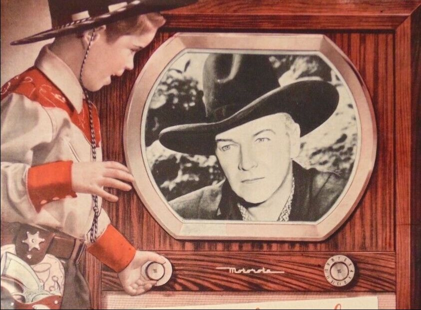 Vintage advertising image of a boy dressed in full cowboy regalia gazing at a black and white image of Hoplong Cassidy on a gargantuan wooden Motorola 16K2 television console with a tiny 16-inch screen.