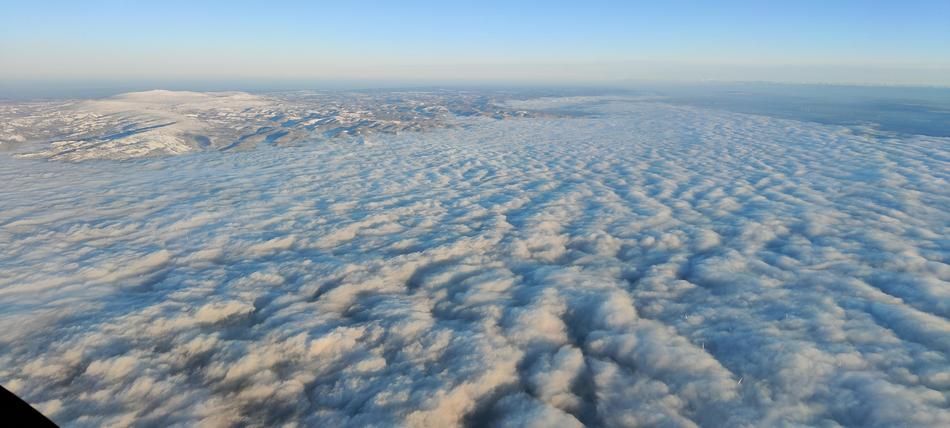 Airial View of clouds and a sole snow covered mountain. 