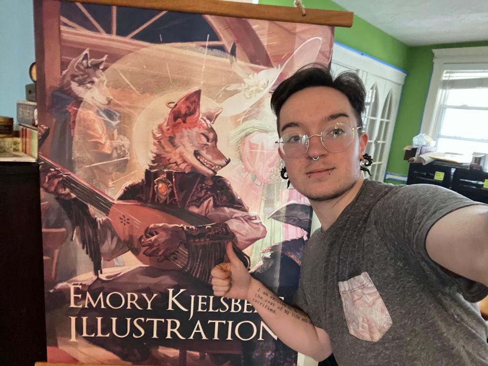 Emory giving an awkward thumbs up in front of a banner for his upcoming booth at the Brighton Bazaar holiday stroll. The banner features his grinning coyote with the lure, haloed in sparkling gold light.