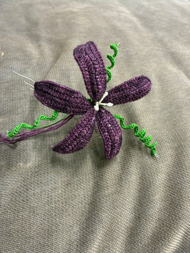 5 petalled, purple, crochet flower with 3 green, spiral, tendrils. 