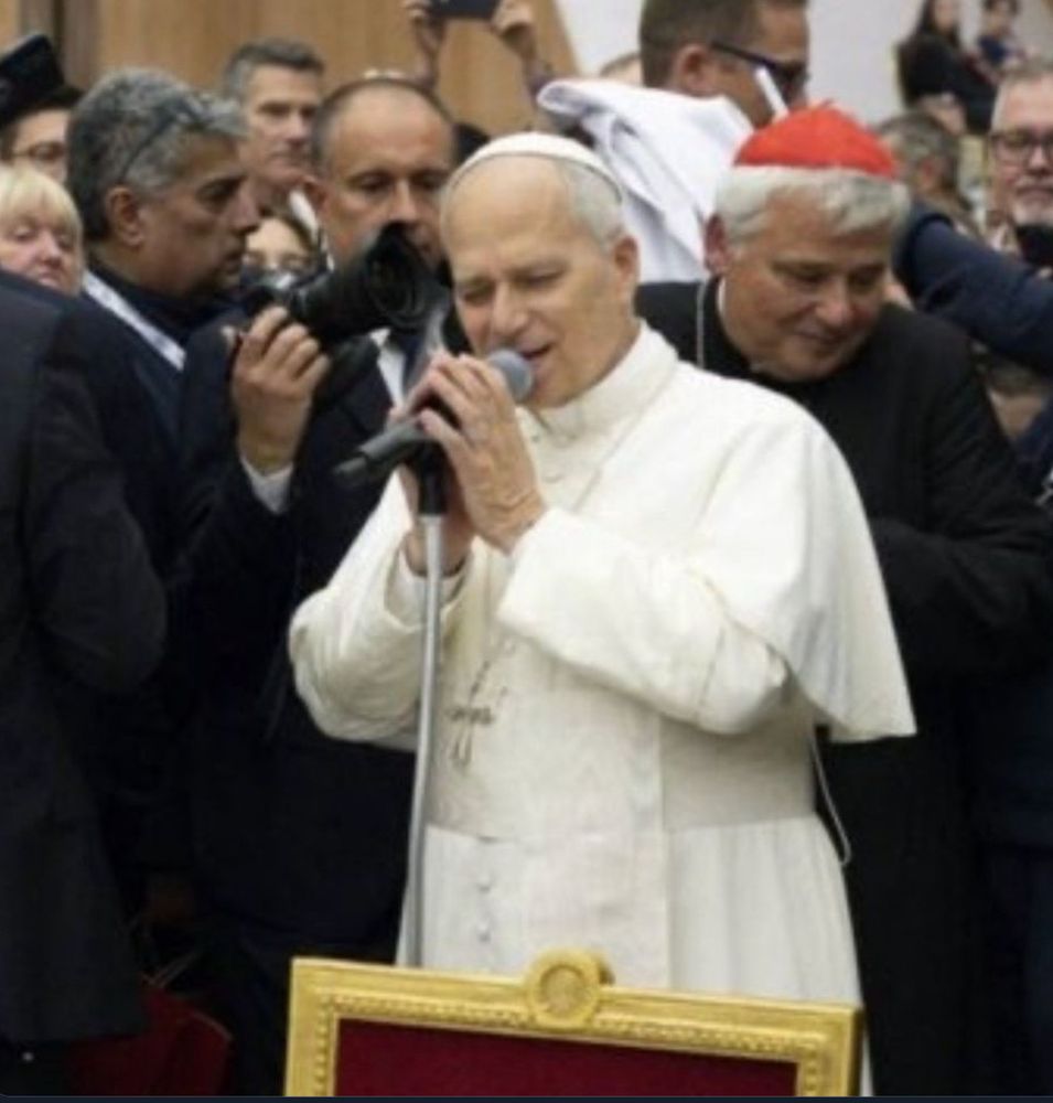 Image of the Pope, with eyes closed, holding a microphone with both hands, making it appear as if he is singing