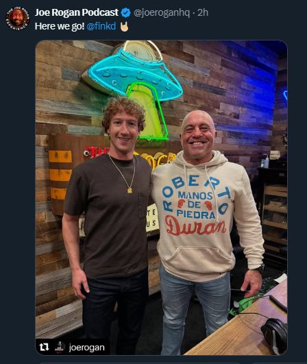 Joe Rogan podcast holding arms with Mark Zuckerberg (ironically a UFO is in the background for someone trying their best to human)