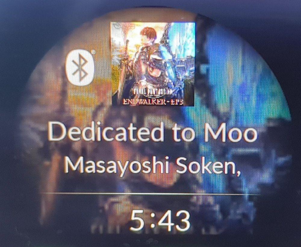 A photo of car dash showing the album art and artist, title of a song. The song title is cut off by a text limit, making an amusing title. "Dedicated to Moo" by Masayoshi Soken with the time displayed below it.